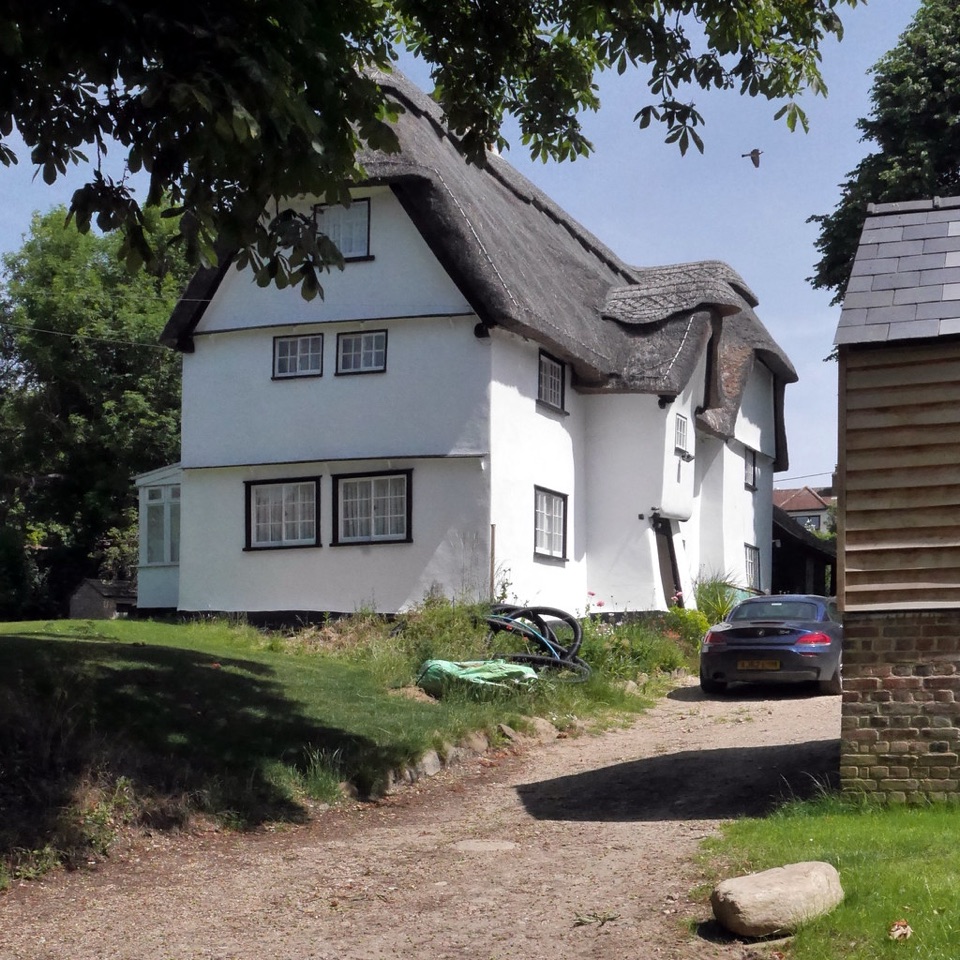 A white rendered thatched farmhouse with a gravel drive at Elsworth in Cambridgeshire