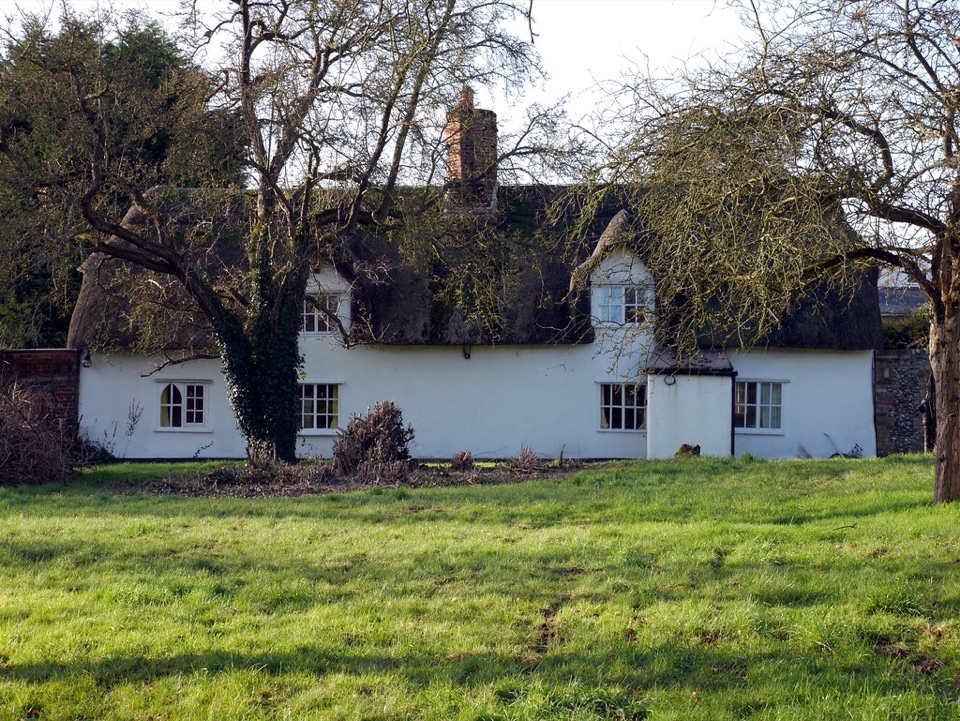 A white thatched cottage standing in open grass at Linton in Cambridgeshire