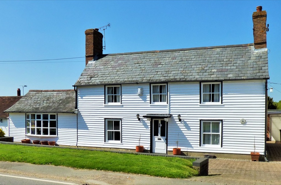 A white weatherboarded house with a slate roof beside a road in England